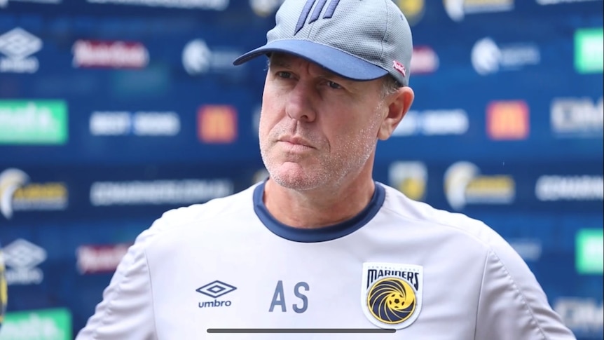 A man in a cap speaks to the media.