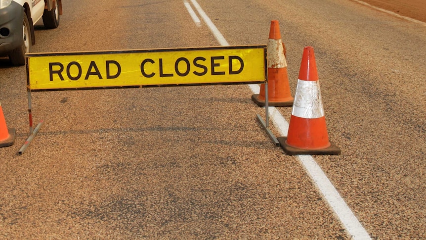 A yellow road closed sign with orange traffic cones