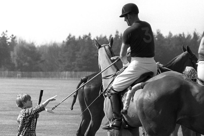 A small boy hands a polo stick to a man on a horse.