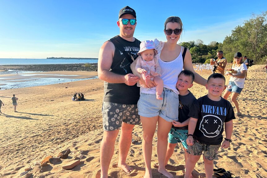 Man, woman and their three kids stand smiling on a beach