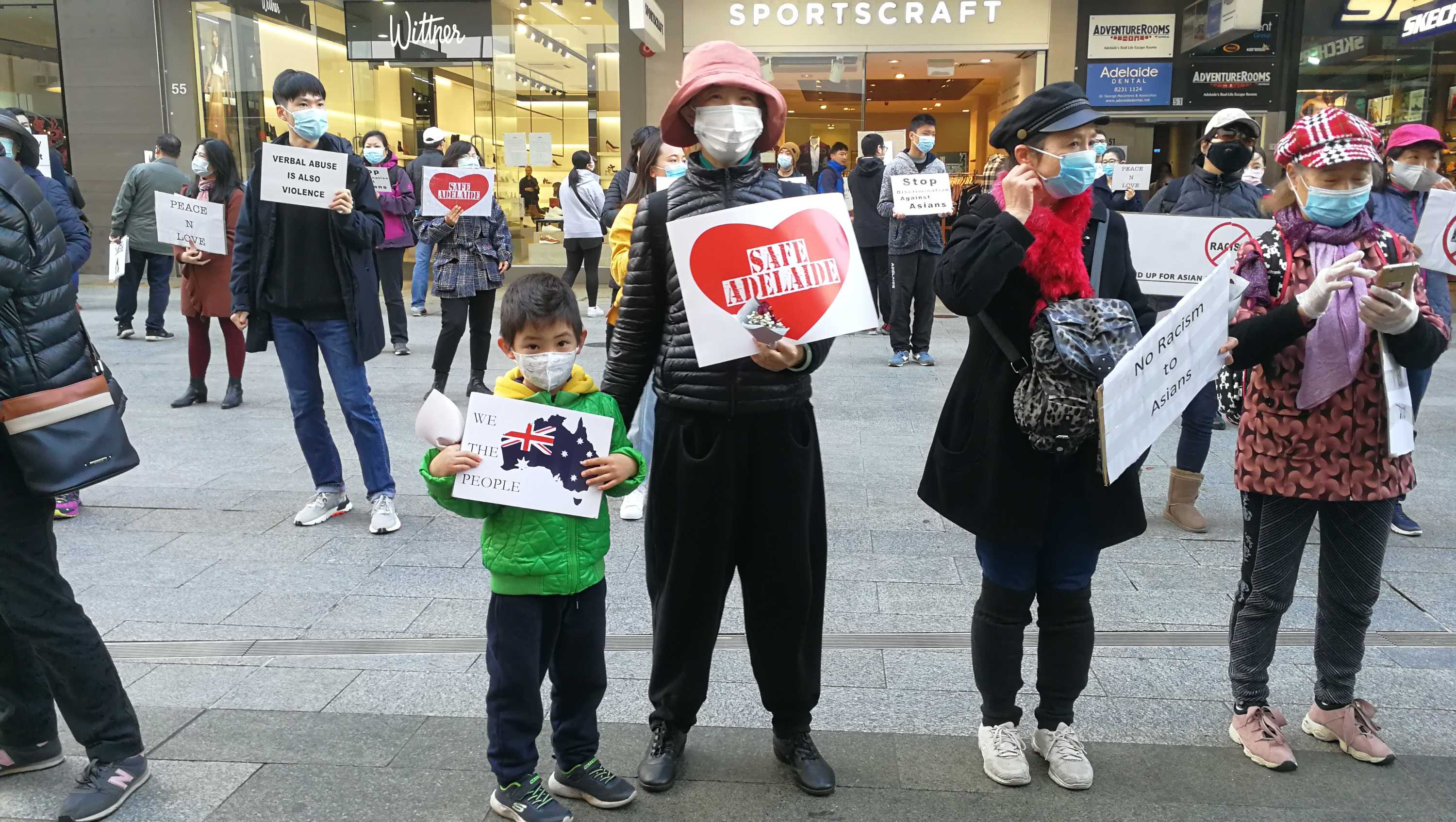 Protesters, wearing face masks, stand around 1.5 metres apart holding signs against racism in Adelaide's CBD.