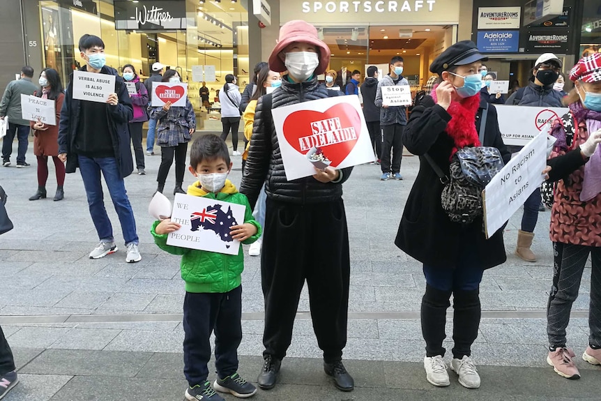 Protesters, wearing face masks, stand around 1.5 metres apart holding signs against racism in Adelaide's CBD.