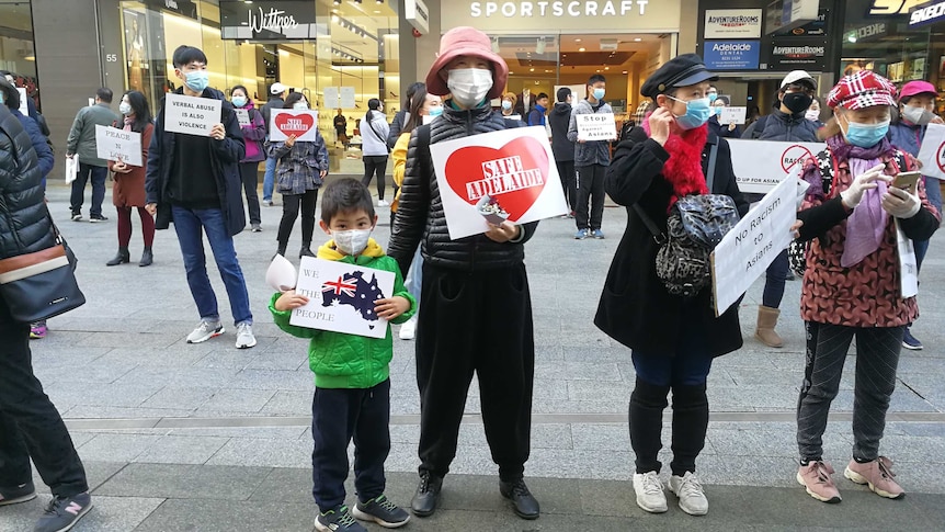 Protesters, wearing face masks, stand around 1.5 metres apart holding signs against racism in Adelaide's CBD.