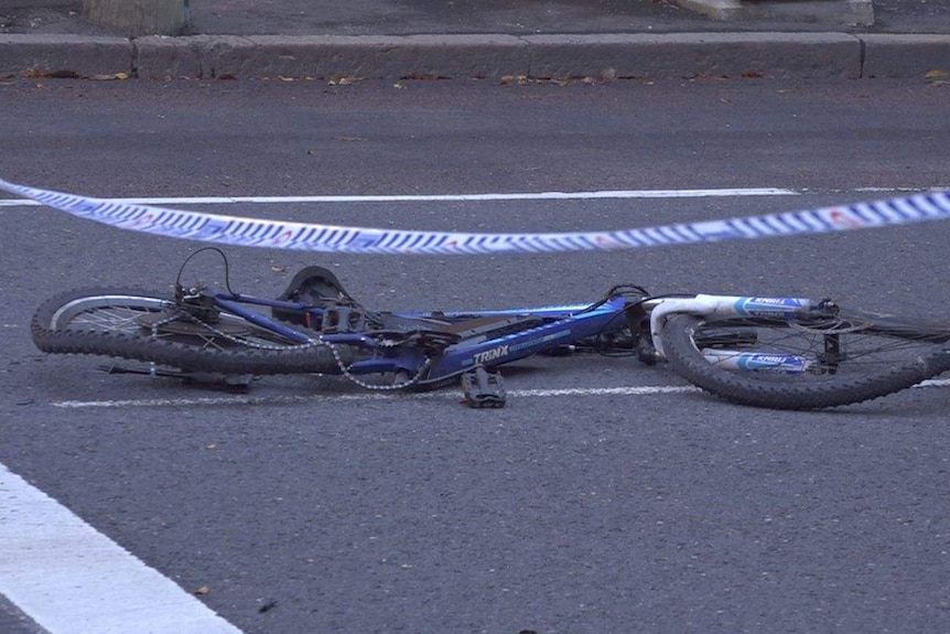 A flattened bike lies on a road with police tape