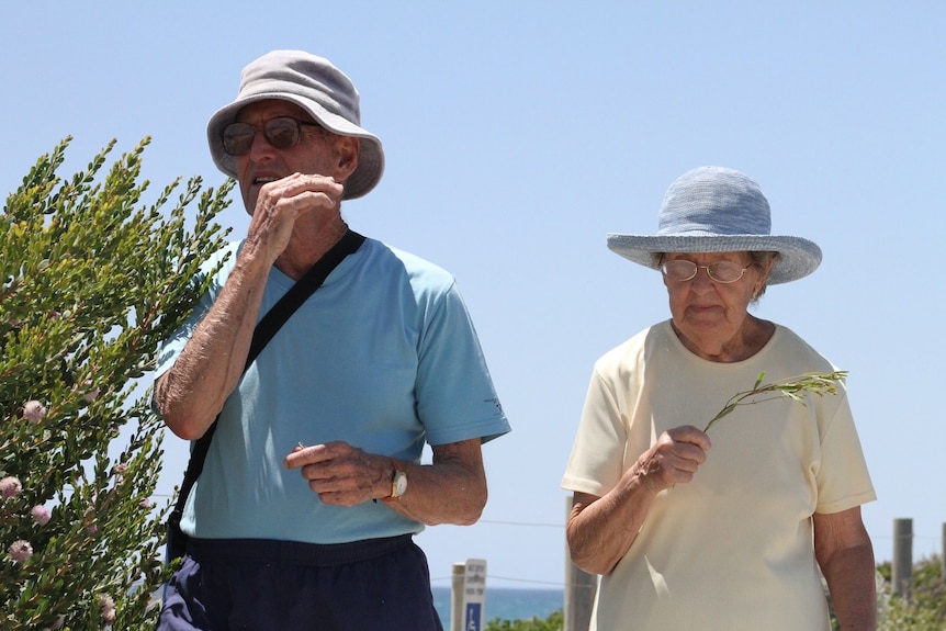 An elderly couple resort to swatting the numerous flies during a walk