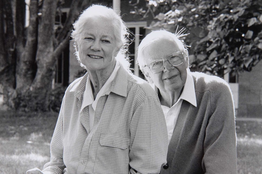 An elderly man and woman sit together looking at the camera.