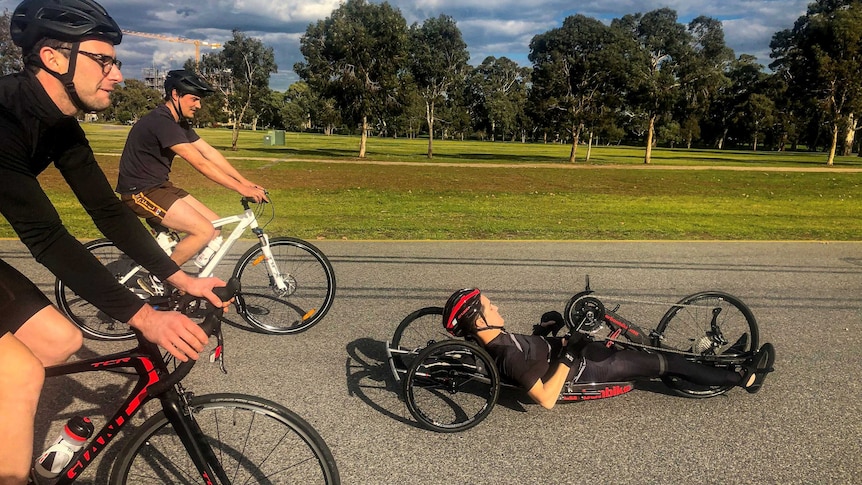 Charles Brice in his handcycling bike with two friends riding bikes behind him