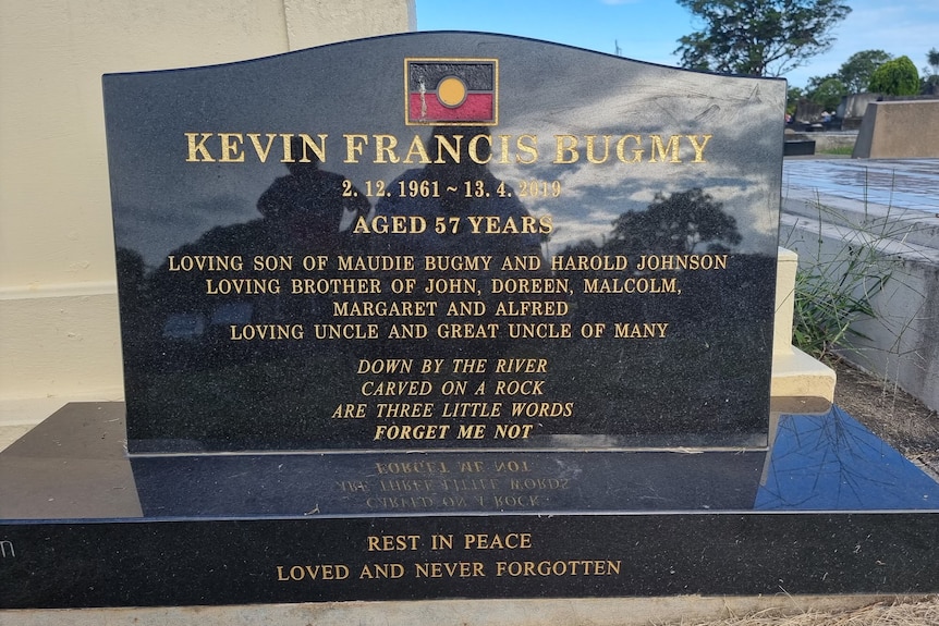 A picture of a black marble gravestone bearing an Aboriginal flag.