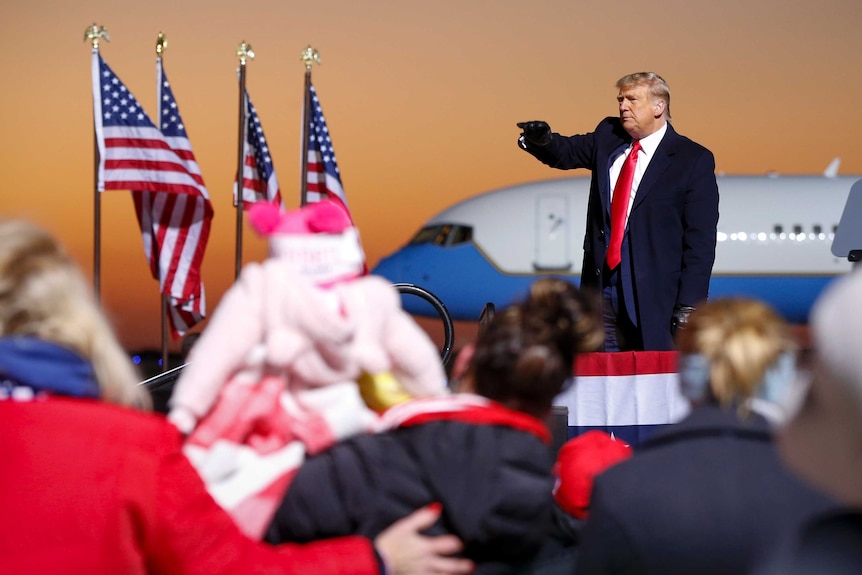 Donald Trump waves from a stage in front of a plane and American flags during an election campaign rally in Rochester Minnesota.