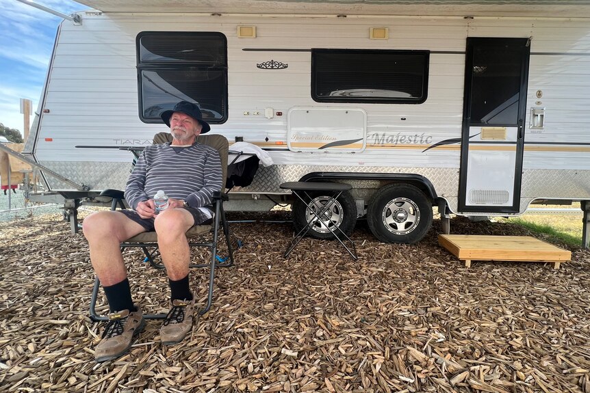 A man sitting on a camping chair in front of a caravan.