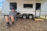 A man sitting on a camping chair in front of a caravan.
