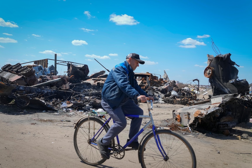A local resident rides a bike past a destroyed Russian military vehicle