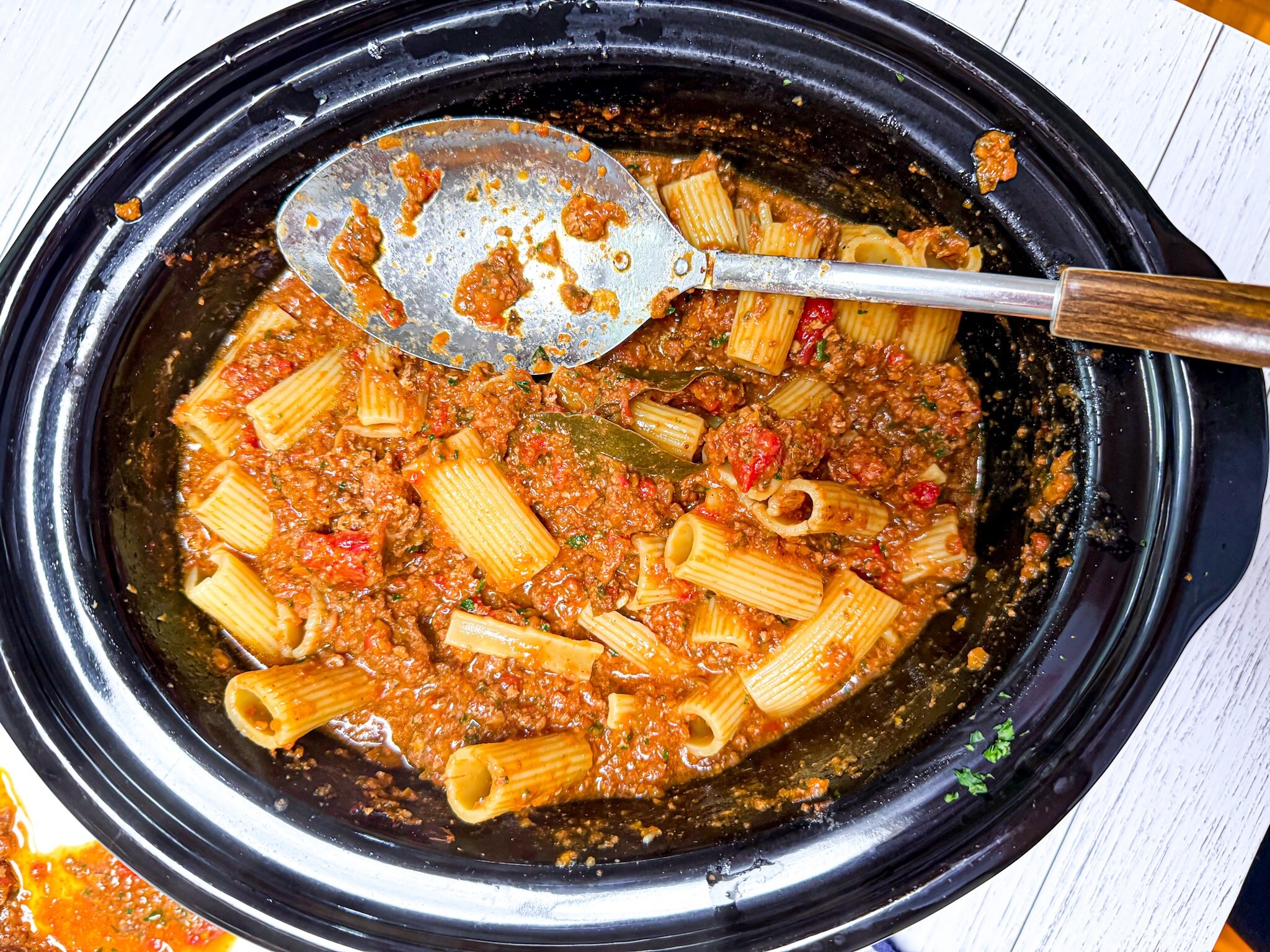 A slow cooker filled with bolognese sauce and cooked rigatoni, ready to serve for dinner. An easy make-ahead meal for busy we