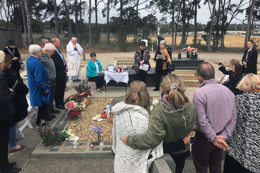 Mourners stand around a mass grave