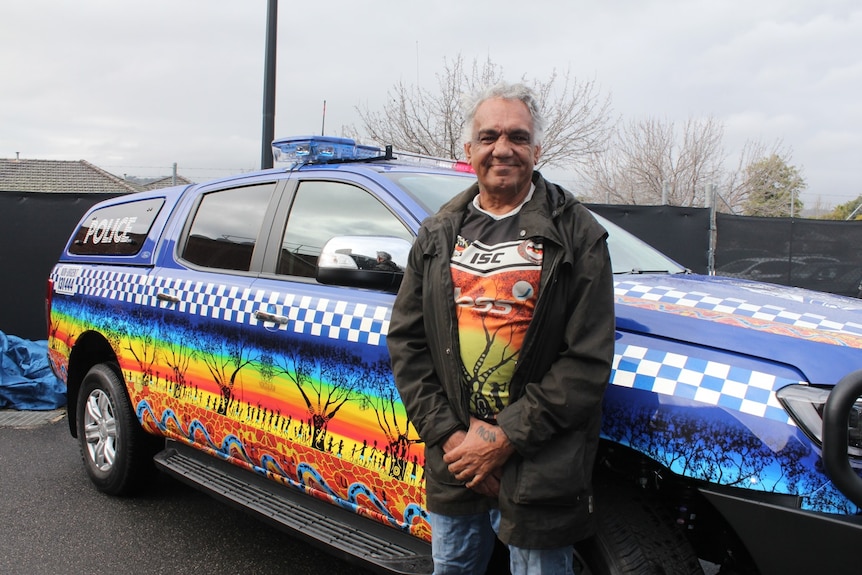 A man stand in front of a police car that is colourfully painted