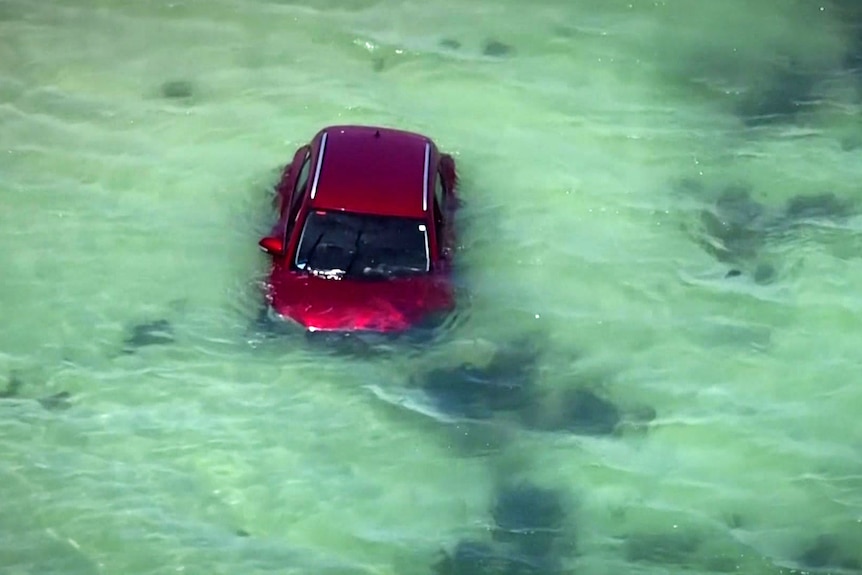 A red car floats in shallow water