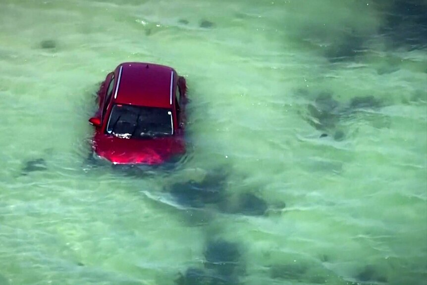 A red car floats in shallow water