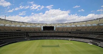 A wide shot of the grassed grounds and tiered seating at Perth Stadium with a blue sky.