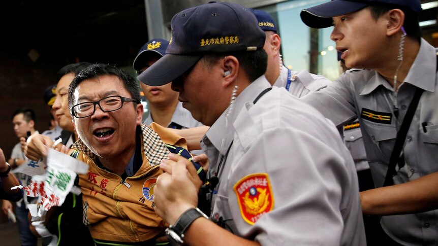 An anti-China protester wearing a yellow jacket is apprehended by four police officers.