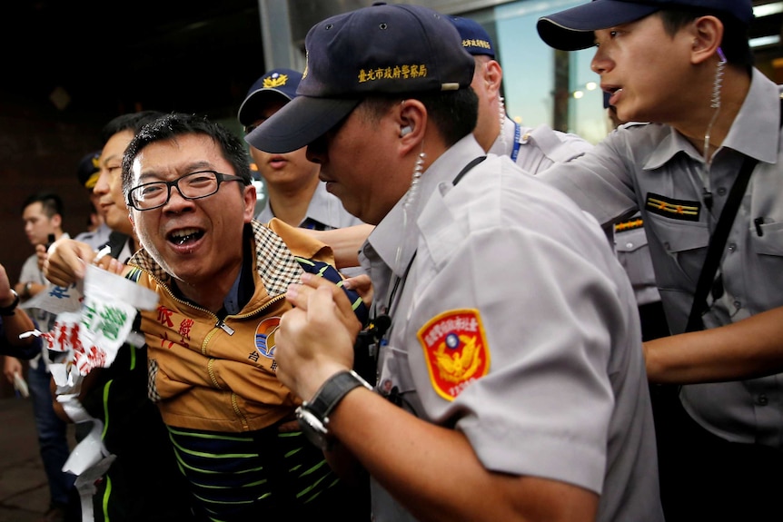 An anti-China protester wearing a yellow jacket is apprehended by four police officers.