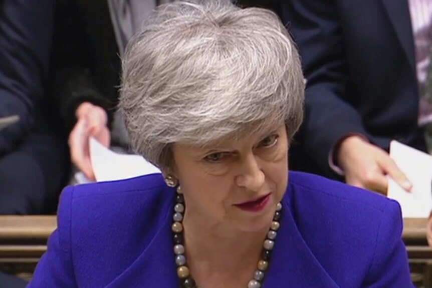 Theresa May, wearing a blue jacket, speaks in the House of Commons
