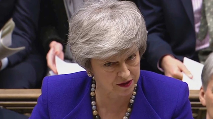 Theresa May, wearing a blue jacket, speaks in the House of Commons