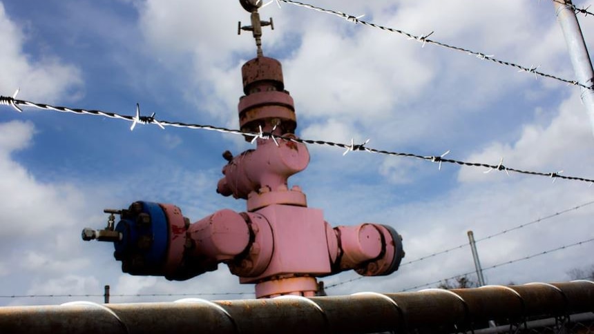 Faded red gas well head behind barbed wire fence