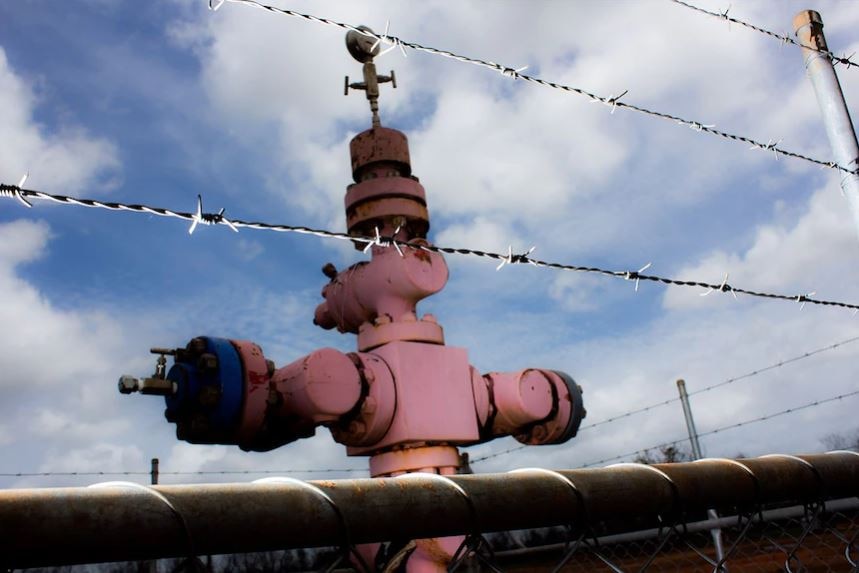 Faded red gas well head behind barbed wire fence