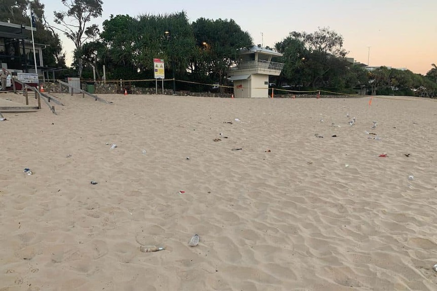 Glass bottles and rubbish strewn on a beach at sunrise