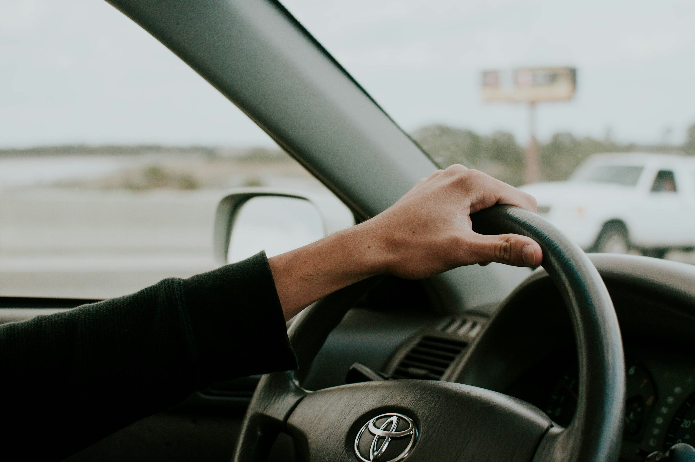 A photo inside a Toyota, with a person's arm and hand on the steering wheel.