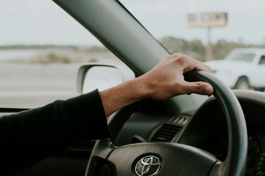 A photo inside a Toyota, with a person's arm and hand on the steering wheel.