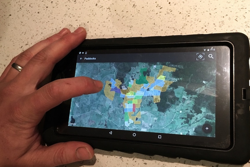 A hand touching a tablet device with an aerial photo of his farm