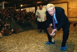 Boris Johnson crouches over holding a chicken during a visit to a chicken farm in Wales.