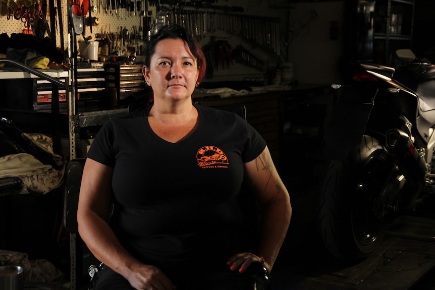 Mechanic Sharine Milne poses in front of Spanners with a black tshirt and moody lighting.