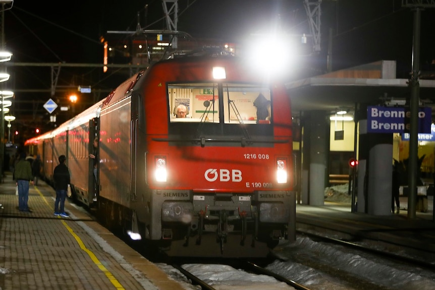 A red train stops at a platform at the Brenner Pass in Italy.