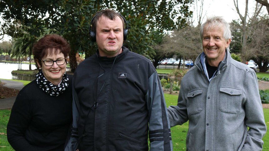 A woman standing next to two men, with the man in the middle wearing headphones.