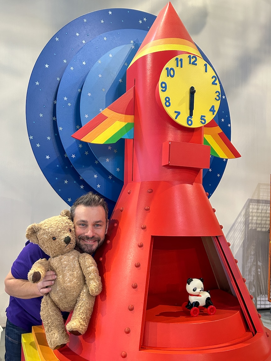 a smiling man with a toy rocket clock