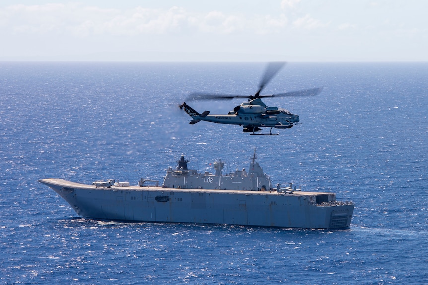 A helicopter flies over a ship on open water.