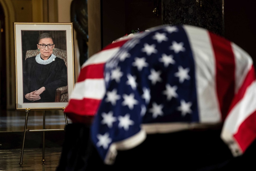 The flag-draped casket of Justice Ruth Bader Ginsburg and a portrait.