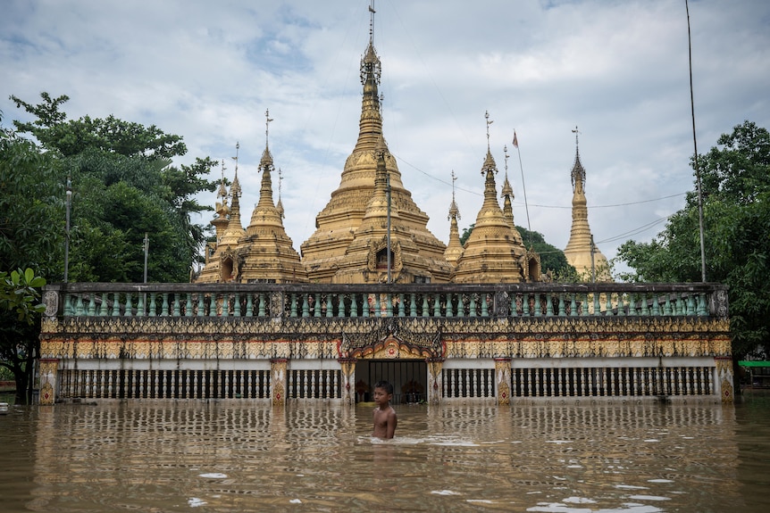 A boy wades in hip-deep flood water with a pagoda in the background. 