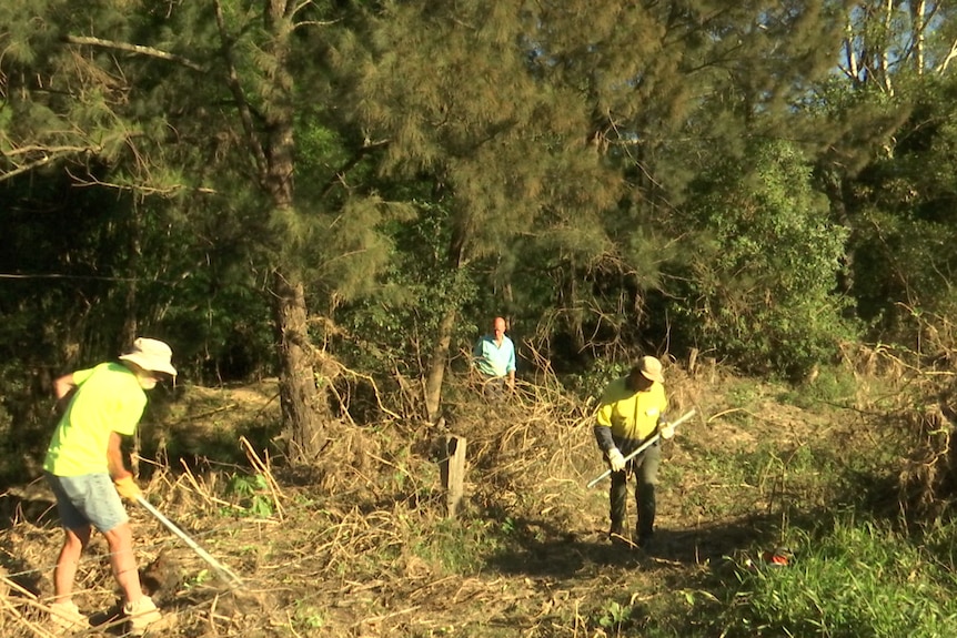 Three volunteers clear debris with chainsaws and shovels on a farm