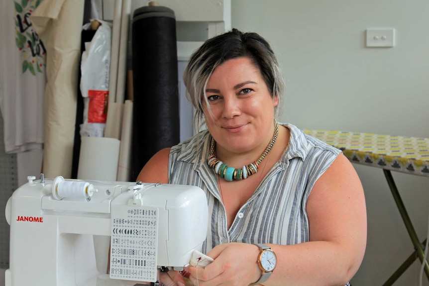 A woman sitting by a sewing machine and smiling