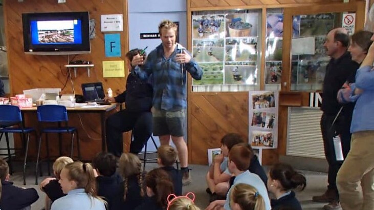Andrew Powell stands in front of a classroom of children delivering a speech.