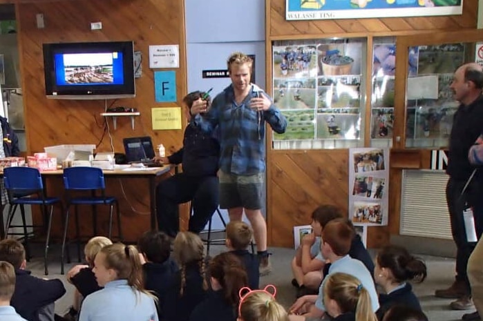 Andrew Powell stands in front of a classroom of children delivering a speech.