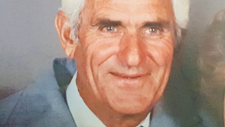 An older man dressed in a suit poses for a family portrait.
