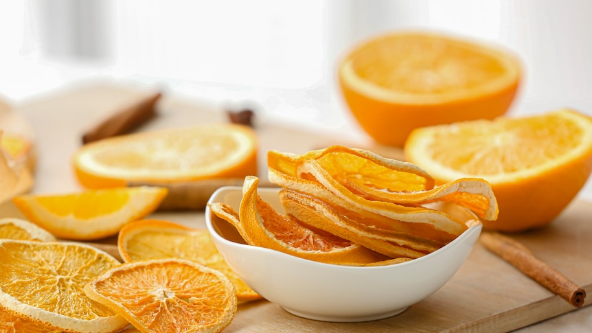 Vivid orange dried orange slices sit in a white bowl.   