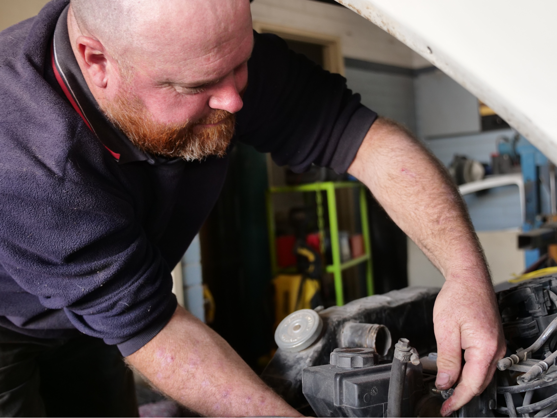 A man with a beard fixing a car