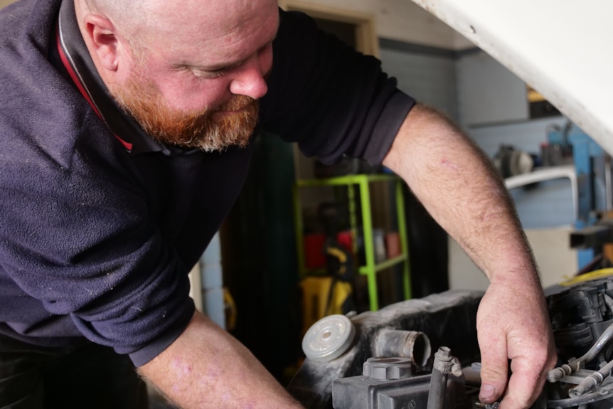 A man with a beard fixing a car