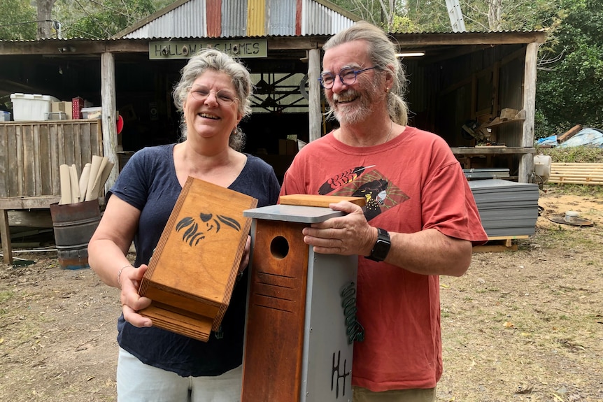 Stacey and Alan Franks laugh as they hold up wildlife nest boxes with a tin shed in the background.