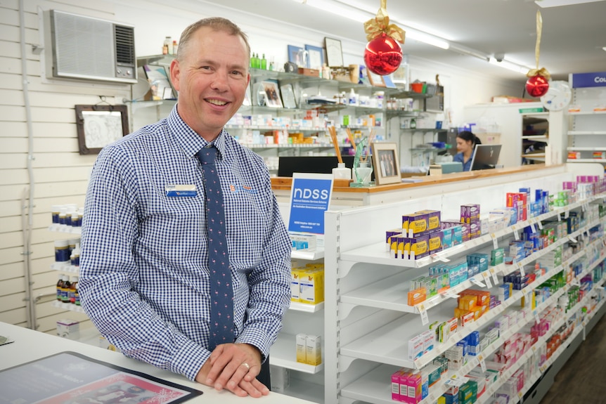 A man standing in front of counter, there is medicine in background